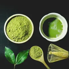 Miska z zielonym proszkiem matcha, filiżanka napoju, drewniana łyżka i bambusowa miotełka.