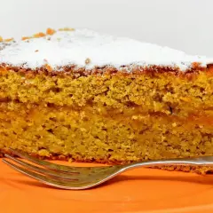 Wilgotne ciasto marchewkowe, posypane cukrem pudrem, idealne jako ciasto dla cukrzyków. Obok leży widelec.