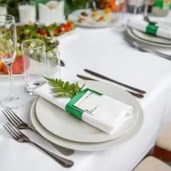 Elegancko nakryty stół: widelce po lewej, nóż po prawej, serwetka z zieloną wstążką i gałązką. Tak ułożyć sztućce, by zachwycić gości.