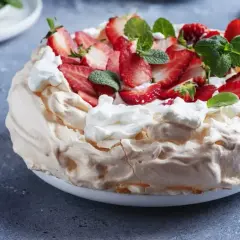 Pyszny tort bezowy z mascarpone i bitą śmietaną, ozdobiony świeżymi truskawkami i miętą.