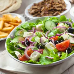 Świeża sałatka z sałatą, pomidorami, ogórkiem, fetą i oliwkami – idealne co do sałatki gyros. Obok frytki i mięso gyros.