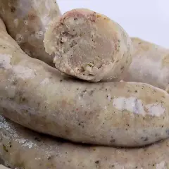 Biała kiełbasa przepis na 3 kg. Gruba, domowa biała kiełbasa, jedna przekrojona, ukazująca wilgotne wnętrze z kawałkami mięsa i przypraw.