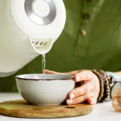 Przygotowanie napoju. Gorąca woda z czajnika leje się do miseczki z zielonym proszkiem. To właśnie co to jest matcha, przygotowywana z pomocą bambusowej miotełki.