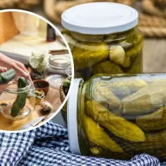 Przygotowanie ogórków kiszonych. W tle słoiki z ogórkami, a na pierwszym planie ręce wkładające ogórka do słoika. Dowiedz się, ile pasteryzować sałatkę z ogórków.
