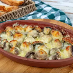 Pyszne pieczarki z piekarnika zapieczone pod ciągnącym serem, podane w glinianym naczyniu. Idealne z chrupiącą bagietką.