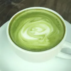Zielony, spieniony napój w białej filiżance na spodku. To matcha latte, co to za napój?