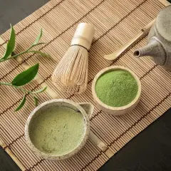 Tradycyjne akcesoria do parzenia matcha: bambusowa miotełka, czarka z napojem, drewniana miseczka z zielonym proszkiem.