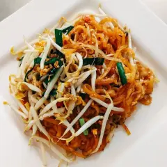 Pad Thai z makaronem ryżowym, kiełkami fasoli mung, jajkiem i szczypiorkiem na białym talerzu.