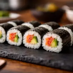 Roladki sushi z łososiem i awokado na czarnej desce.