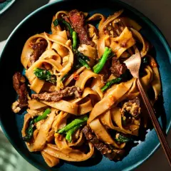 Pad Thai z wołowiną, makaronem ryżowym i zielonymi warzywami na talerzu.