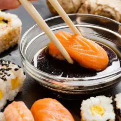 Chopsticks zanurzają kawałek łososia w sosie sojowym do sushi. Obok widać różne rodzaje sushi i imbir.