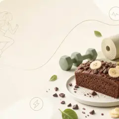 Ciasto z płatków owsianych i bananów z kakao, ozdobione plasterkami banana i kawałkami czekolady. Obok leżą hantle i mata do jogi, a w tle sylwetka biegaczki.