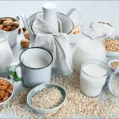 Mleko roślinne w dzbankach i szklankach, obok migdałów, owsa, soi i ryżu.