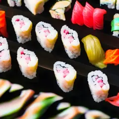 Różnorodne sushi i dodatki ułożone na czarnym tle.