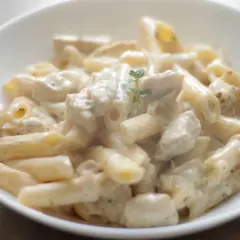 Penne z kurczakiem w kremowym sosie śmietanowo-serowym, udekorowane gałązką ziół. Pyszne danie obiadowe.