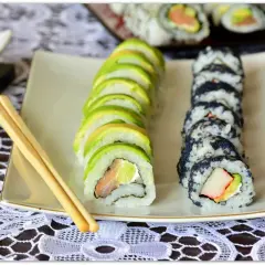 Jak pokroić awokado do sushi? Na talerzu sushi z awokado i czarnym kawiorem, obok pałeczki.