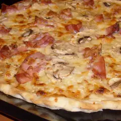 Pyszna pizza carbonara z chrupiącym boczkiem i pieczarkami, obficie posypana serem.