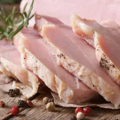 Kawałki super delikatnego i soczystego schabu gotowanego, przyprawione pieprzem, z gałązką rozmarynu i ziarnami pieprzu na drewnianym blacie.