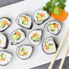 Jak ugotować ryż do sushi? Na talerzu ułożone rolki sushi z awokado, ogórkiem i marchewką. Obok pałeczki i dekoracja z wasabi.