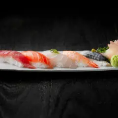 Pięć kawałków sushi z rybą, krewetką i dodatkami na białym talerzu.