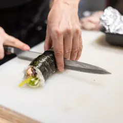 Dłonie kroją rolkę sushi. Zastanawiasz się, czy sushi można zamrozic? Ten obrazek pokazuje przygotowanie świeżego sushi.