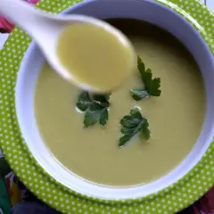 A spoonful of zupa krem z brokułów z ziemniakami, garnished with parsley, sits in a green polka-dot bowl on a floral placemat.