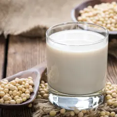 Szklanka mleka sojowego i łyżka ziaren soi. Czy mleko sojowe ma gluten? Nie, jest bezglutenowe.