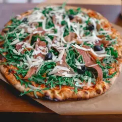 Pyszna pizza prosciutto z rukolą, oliwkami i parmezanem, podana na papierze.