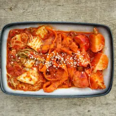 Gotowe kimchi z kapusty pekińskiej, z marchewką i sezamem, na drewnianym tle. Idealne do nauki jak zrobić kimchi z kapusty pekińskiej.