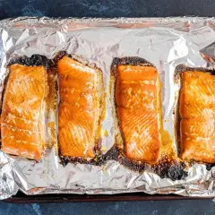 Cztery kawałki łososia na blasze wyłożonej folią aluminiową, gotowe do przygotowania sushi.