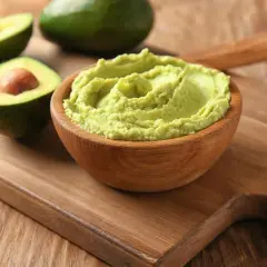 Gotowe guacamole w drewnianej misce, obok przekrojone awokado. Idealne do nauki, jak zrobić guacamole.