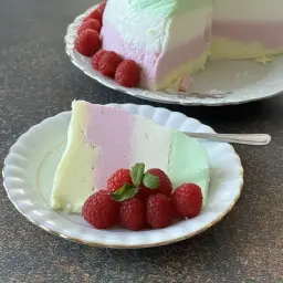 Kolorowy jogurtowiec z jogurtu greckiego, udekorowany malinami i miętą, na talerzyku.