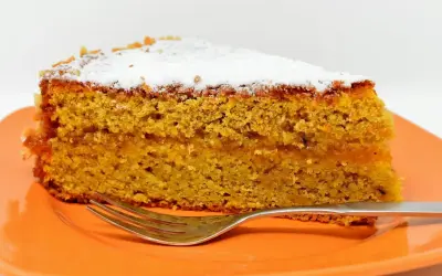 Wilgotne ciasto marchewkowe, posypane cukrem pudrem, idealne jako ciasto dla cukrzyków. Obok leży widelec.