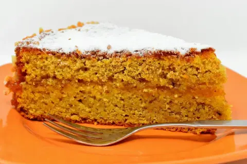 Wilgotne ciasto marchewkowe, posypane cukrem pudrem, idealne jako ciasto dla cukrzyków. Obok leży widelec.