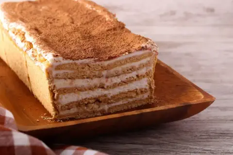 Tanie ciasto bez pieczenia z herbatnikami, przełożone kremem i posypane kakao. Idealne na szybki deser.