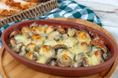 Pyszne pieczarki z piekarnika zapieczone pod ciągnącym serem, podane w glinianym naczyniu. Idealne z chrupiącą bagietką.