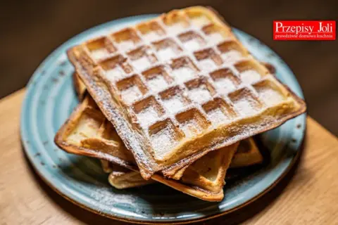 Stary przepis na gofry, lekko oprószone cukrem pudrem, kuszą na talerzu. Idealne na leniwe śniadanie.