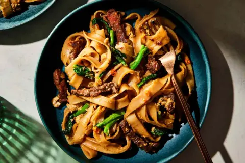 Pad Thai z wołowiną, makaronem ryżowym i zielonymi warzywami na talerzu.
