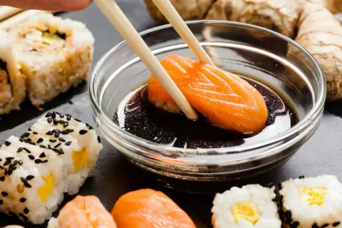 Chopsticks zanurzają kawałek łososia w sosie sojowym do sushi. Obok widać różne rodzaje sushi i imbir.
