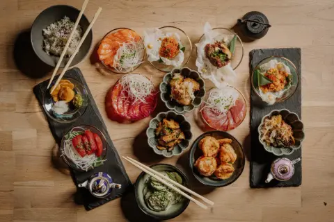 Pyszne sushi w Szczecinie czeka! Na stole różnorodne dania: łosoś, tuńczyk, krewetki, ryż i dodatki. Idealne na wspólne jedzenie.