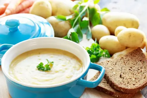 Aksamitna, tradycyjna zupa ziemniaczana w niebieskiej miseczce, udekorowana natką pietruszki. Obok kromki ciemnego chleba i świeże ziemniaki.
