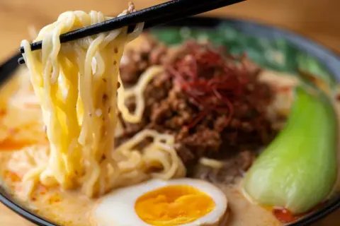Jak zrobić ramen z zupki chińskiej? Miska pełna pysznego ramenu z makaronem, mięsem mielonym, jajkiem i warzywami.