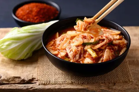 Miseczka pełna pikantnego kimchi, idealnego dodatku do wielu dań. Obok kapusta i chili.