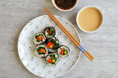 Roladki sushi z warzywami na talerzu, pałeczki i sosy. Tak przygotować nori do sushi, by było pyszne!