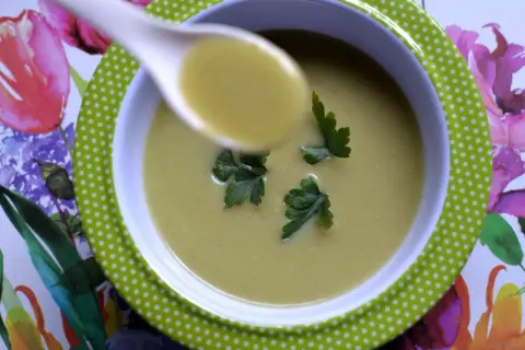 A spoonful of zupa krem z brokułów z ziemniakami, garnished with parsley, sits in a green polka-dot bowl on a floral placemat.