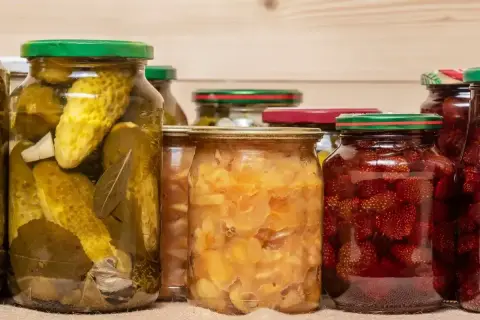 Słoiki z ogórkami, truskawkami i innymi przetworami, gotowe do wekowania w piekarniku.