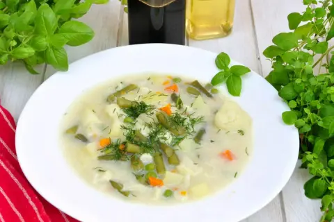 Aromatyczna, tradycyjna zupa jarzynowa z ziemniakami, fasolką szparagową, kalafiorem i groszkiem, udekorowana świeżym koperkiem.
