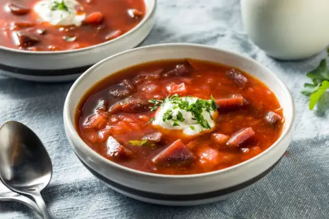 Dwie miseczki aromatycznej zupy z botwiny na mięsie, ozdobione kleksem śmietany i posiekaną natką pietruszki.