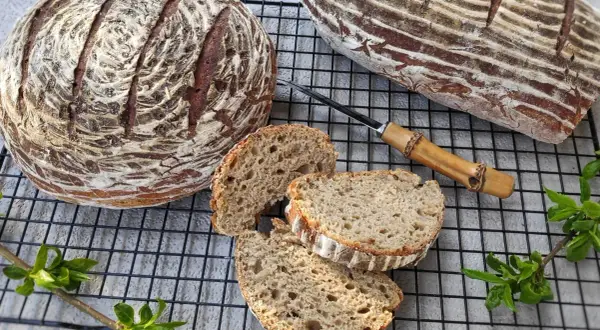 Dwa bochenki chleba żytniego na zakwasie, jeden okrągły, drugi podłużny, z kilkoma kromkami obok.
