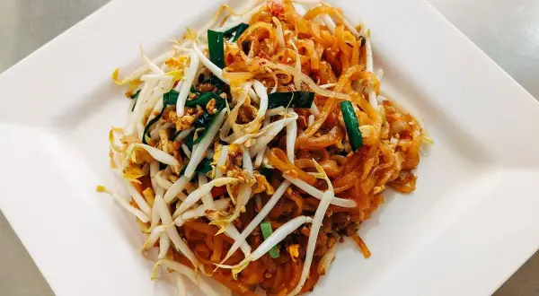 Pad Thai z makaronem ryżowym, kiełkami fasoli mung, jajkiem i szczypiorkiem na białym talerzu.